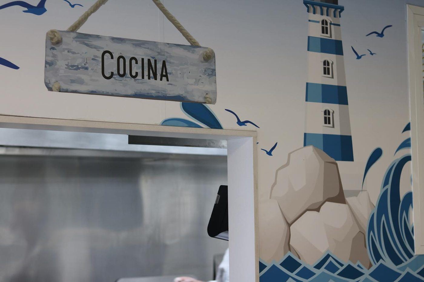 Cartel de cocina colgado junto al mural del faro en La Victoria